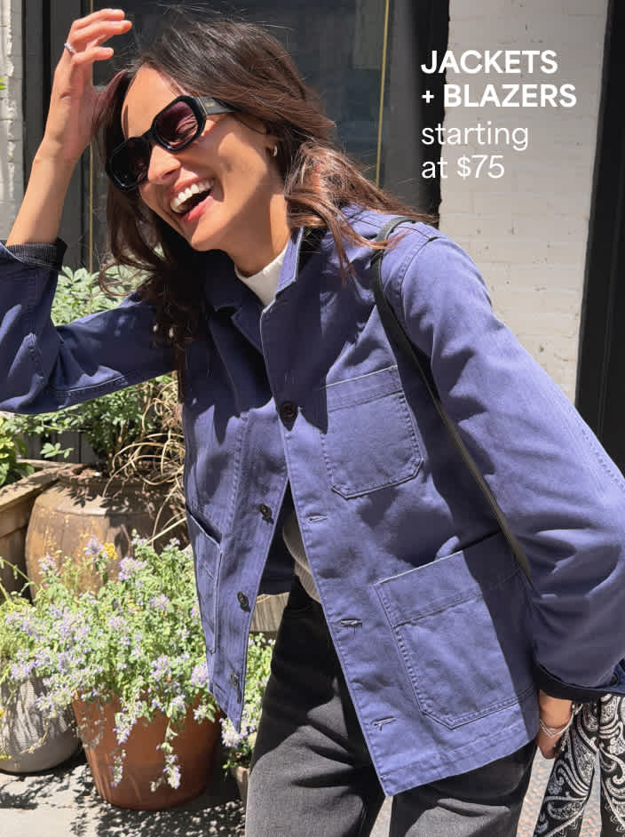 Woman wearing blue button-down jacket with pockets, black pants, sunglasses, and holding black handbag