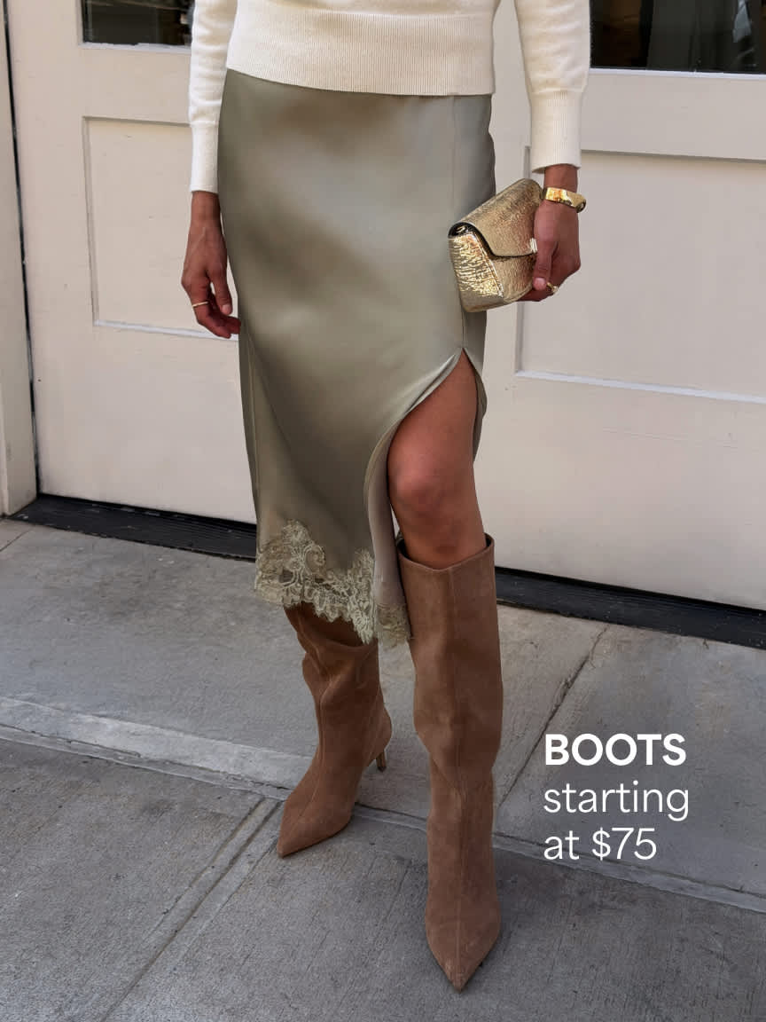 A cropped photo of a woman standing on a city sidewalk highlighting her footwear, featuring tall tan suede pointed-toe boots paired with a champagne satin midi skirt with a side slit and a gold metallic clutch bag. Text overlay reads "BOOTS starting at $75".