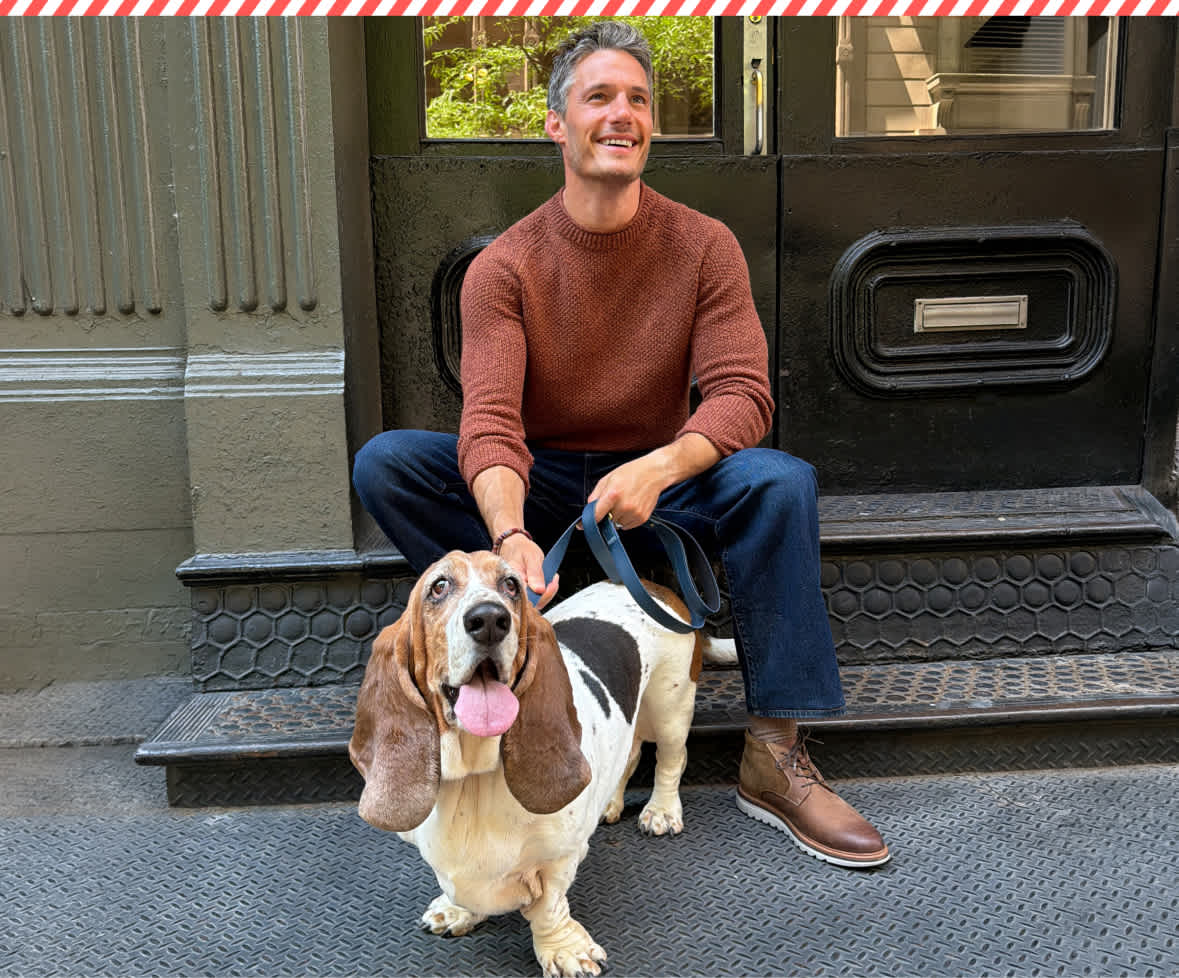 A split holiday image showing a man in a white sweater and a woman in a red sweater standing next to a Christmas tree on a city sidewalk on the left, and a man in a rust-colored sweater sitting on stone steps holding a basset hound on a leash on the right.