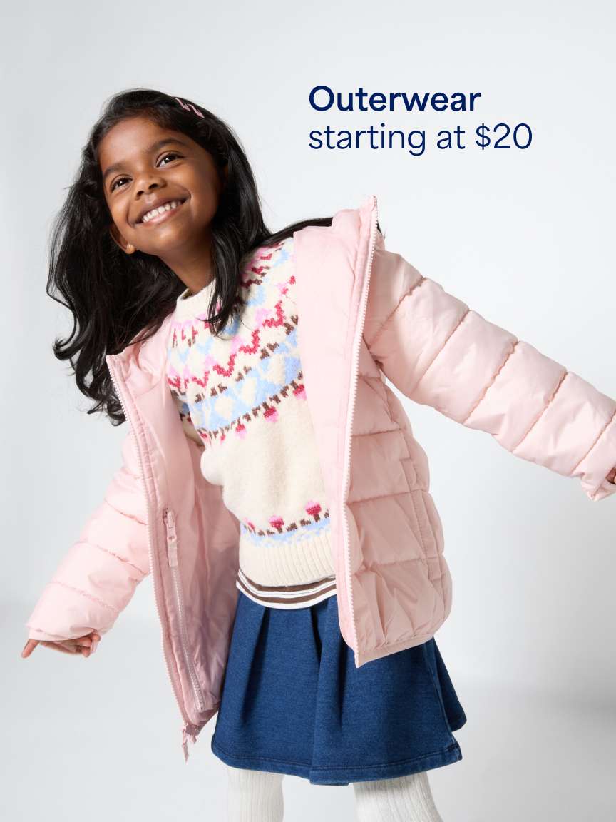 A smiling young girl wearing a light pink puffer jacket over a fair-isle sweater and a blue pleated skirt with white tights. Text overlay reads "Outerwear starting at $20".