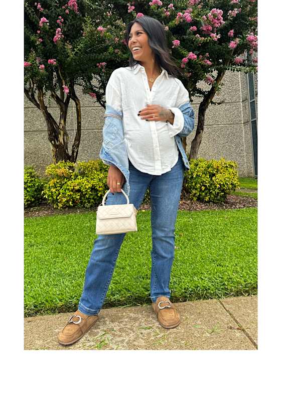 Maternity model wearing Stitch Fix women’s clothing, including: a white button-down shirt, blue jeans, and moccasins, holding a small cream-colored handbag and smiling.