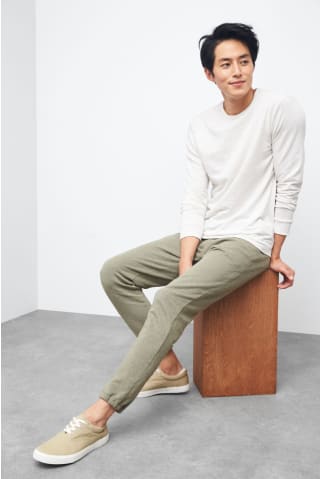 Model wearing Stitch Fix mens Mohnton Made clothing including a light colored long sleeve t-shirt, relaxed olive pants and tan shoes.