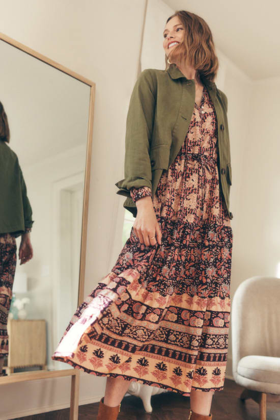 Woman standing in front of home mirror with Stitch Fix outfit of printed midi dress and green army jacket